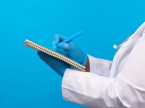 Medic woman in white coat, blue latex gloves holding an open notebook